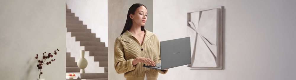 Notebook Asus Zenbook S16 OLED bílý Žena drží v ruce otevřený Zenbook S16 s prémiovým designem pro práci, studium i každodenní používání