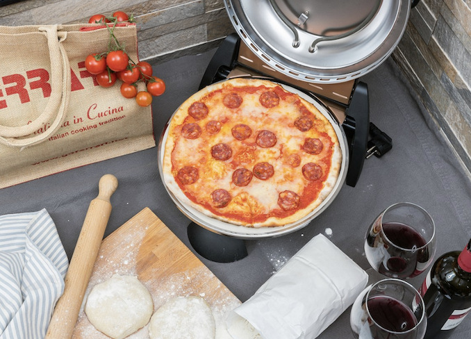 Otevřená pec na pizzu s upečenou pizzou, připraveným těstem a prostřeným stolem