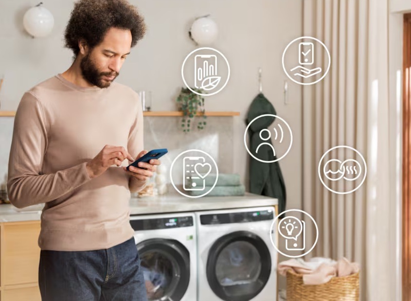 Sušička prádla Electrolux série 800 EW8D595RCDC ocel Muž ovládá sušičku Electrolux pomocí mobilní aplikace. Kolem jsou symboly jednotlivých funkcí.
