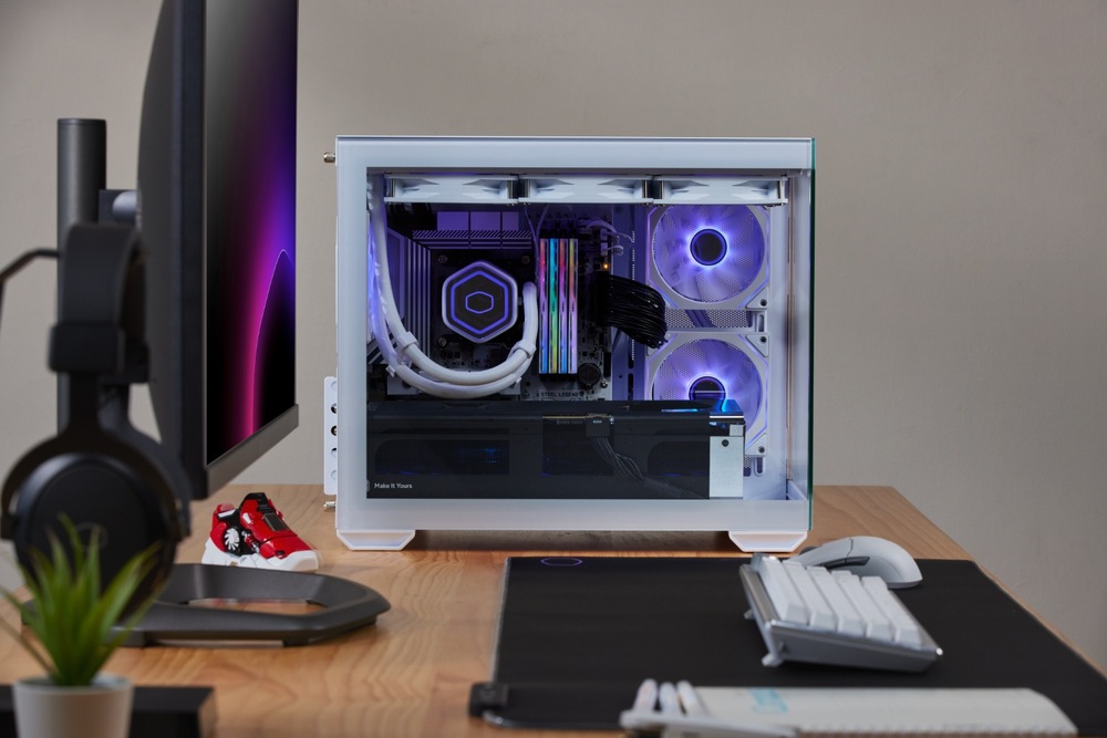 Case Cooler Master Elite 481 Wood ARGB bílá Elegantní bílá počítačová skříň s osazenými komponentami, svítícími fialovými LED ventilátory a kabely na dřevěném stole. Monitor, klávesnice a sluchátka jsou poblíž a vytvářejí moderní sestavu.