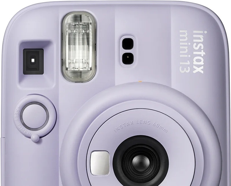Instantní fotoaparát Fujifilm instax mini 13 fialový Detail přední strany fotoaparátu Fujifilm instax mini 13 s indikátorem samospouště vedle objektivu