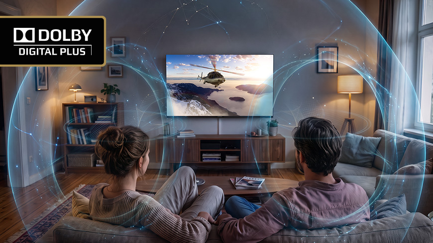 Televize Hyundai HL 327602V Technologie zvuku Dolby Digital Plus: Pár sedící v obývacím pokoji sledovaný prostorovým zvukovým efektem vycházejícím z televizoru. Logo: Dolby Digital Plus
