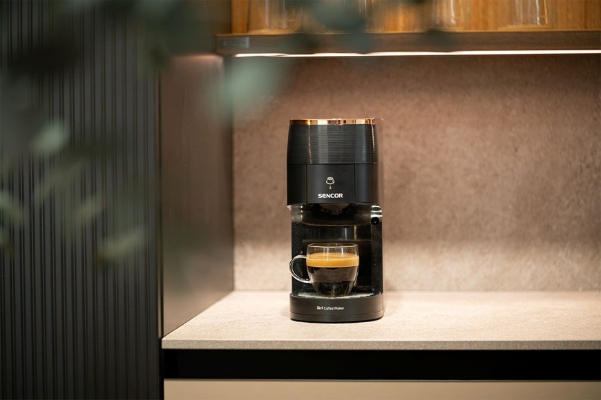 Kapslový kávovar Sencor SCC 3000BK MARCO POLO je položen na moderní kuchyňské lince a právě připravil espresso.