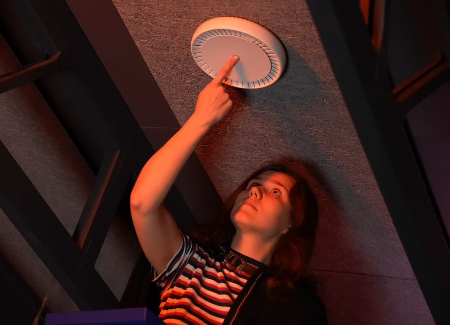 Žena mačkající tlačítko na stropním access pointu MikroTik při instalaci.