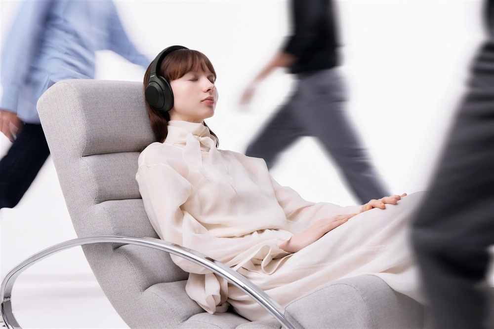 žena se sluchátky Sony WH-1000XM4C při poslechu hudby v křesle