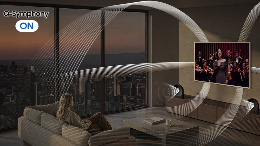 Reproduktory Samsung Music Studio 5 LS50H (2 ks) černé Obývací pokoj s výhledem na město, kde žena sleduje televizi s orchestrem. Je to vizualizace prostorového zvuku s funkcí Q-Symphony zapnutou.