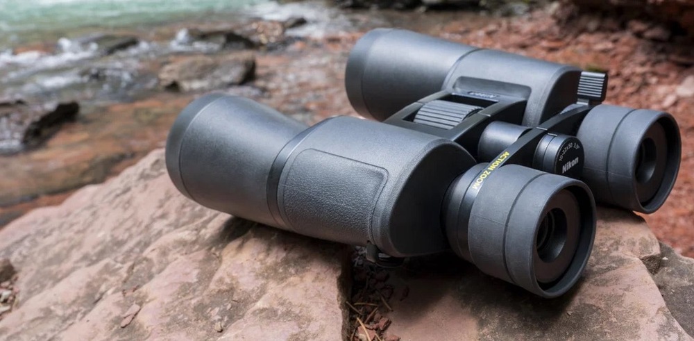 Dalekohled Nikon Action 12×50 černý Dalekohled Nikon Action 12×50 je položen na kamenitém břehu řeky.