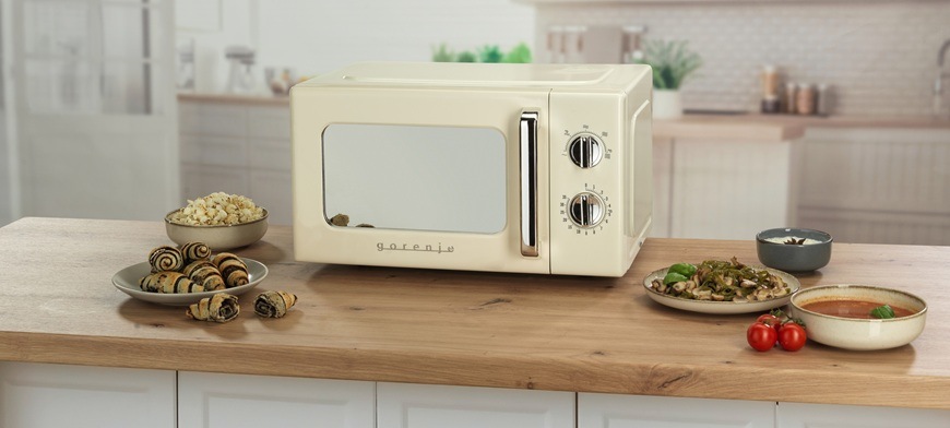 Mikrovlnná trouba Gorenje Retro MO20E1HRL béžová Retro mikrovlnná trouba Gorenje MO20E1HRL má pootevřená dvířka. Je umístěná na kuchyňské lince a kolem ní jsou různé potraviny.