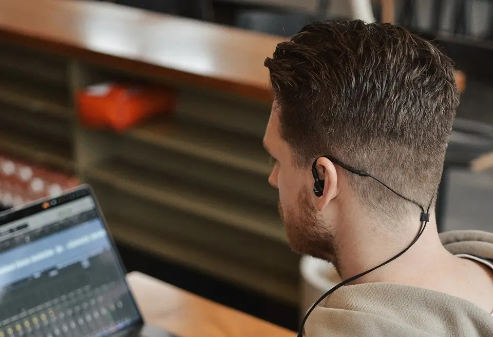 Muž upravující hudbu v notebooku má nasazená sluchátka Beyerdynamic DT 70 IE