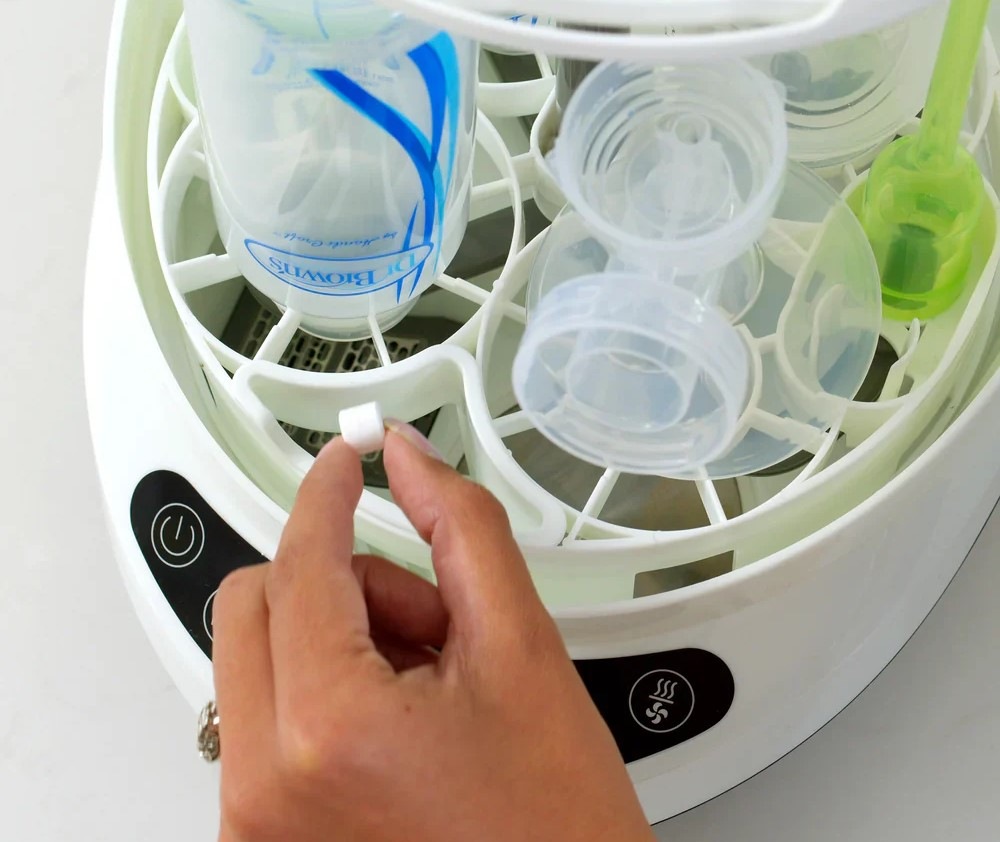 Sterilizátor Baby Brezza Bottle Washer Pro Black černý Detail ženské ruky, která v ruce drží malý čisticí prášek, který lze používat se sterilizátorem Baby Brezza Bottle Washer Pro Black.