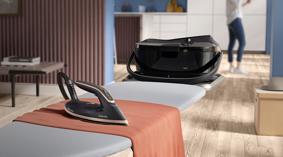 Žehlicí systém Philips 8000 Series PSG8300/80 černý Žehlicí systém Philips PSG8300/80 8000 Series položenž na žehlícím prkně a žena vzdálená v další místnostnosti