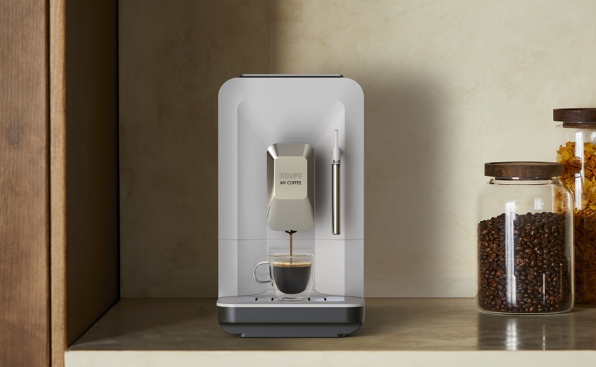 Čelní pohled na automatický kávovar Krups EA201BE0 My Coffee Steam, který je položen na lince. Vedle něj jsou dózy s kávovými zrny.