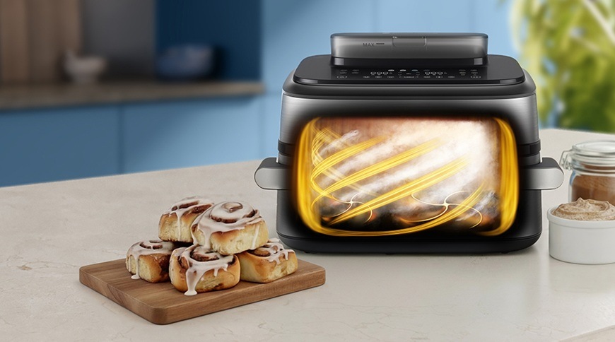 Fritéza horkovzdušná Philips Airfryer Dual Basket s párou 9,5 l NA565/02 černá/stříbrná Horkovzdušná fritéza Philips NA565/02 s průhledem do koše, ve kterém jsou viditelné rotující proudy horkého vzduchu během přípravy pečiva. Vedle spotřebiče na kuchyňské lince leží čerstvě upečené skořicové šneky s polevou.