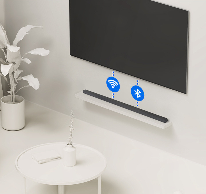 Soundbar Samsung leží na polici pod televizí, mezi ním a televizí jsou dvě tečkované čáry s ikonami Wi-Fi a Bluetooth připojení