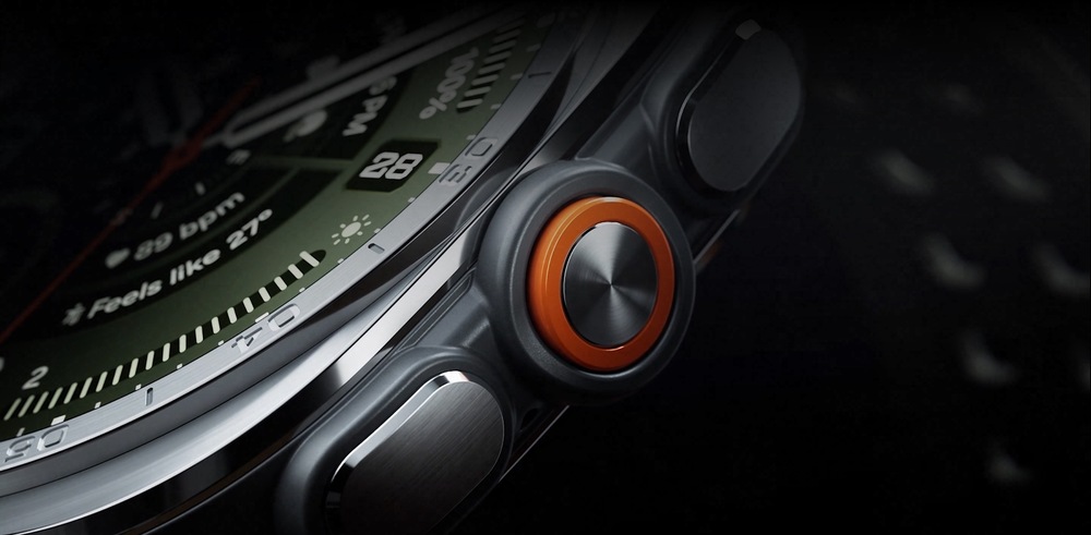 Detailní záběr na odvážně navržená, intuitivní tlačítka a oranžové Akční tlačítko na boční straně hodinek Galaxy Watch Ultra2 v barevném provedení Titanium Silver se sportovním řemínkem Marine Band v barvě Olive zobrazené v mírném úhlu.