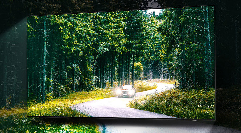 Televize Samsung QE98QN90A Obrazovka televize přes krajinu zachycující cestu v lese, po níž jede auto, obraz pokračuje za obrazovkou