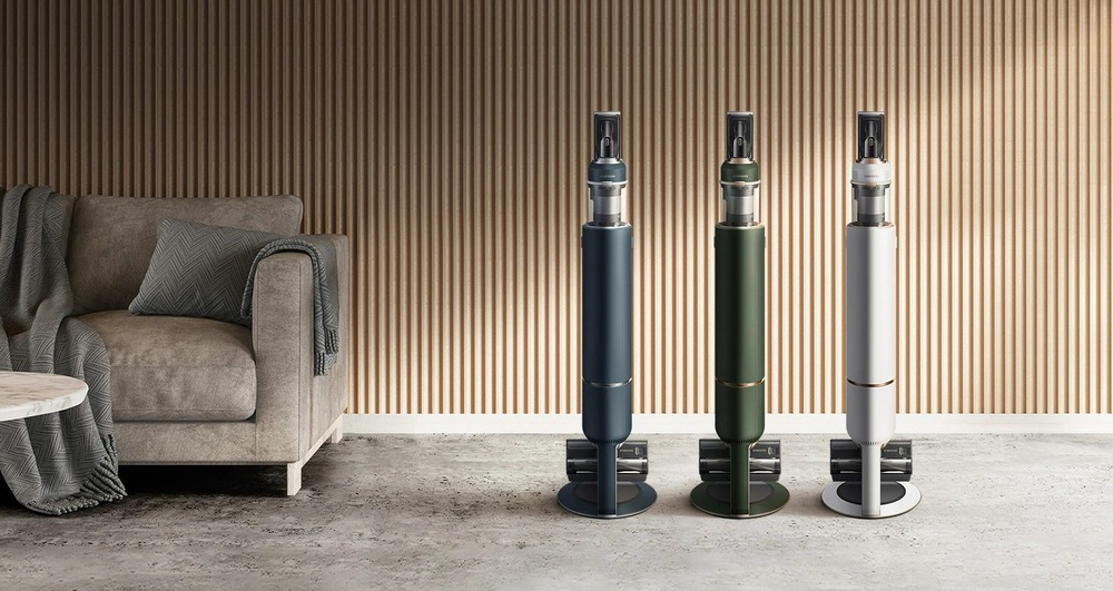 Tyčový vysavač Samsung BESPOKE Jet pet VS20A95823W/GE bílý Tři vysaavče Samsung Bespoke Jet Pet VS0A95823W/GE v různém barevném provedení (modrém, zeleném a bílém) stojí vedle sebe v obývacím pokoji, vlevo je pohovka se stolkem