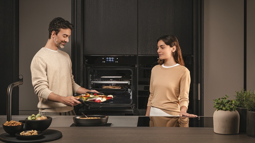 žena a muž stojí v kuchyni, muž dává pekáč s jídlem do trouby Haier H6 ID48C5YTB. na lince je další pekáč s masem a sondou preci probe