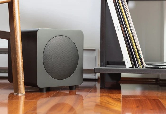 Subwoofer Kanto SUB8 černý Subwoofer Kanto SUB8 je umístěný na zemi vedle dalšího nábytku.
