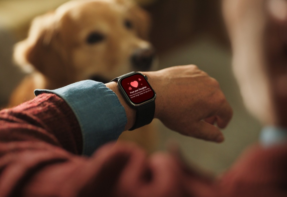 Chytré hodinky Huawei Watch D3 zlaté Detail chytrých hodinek na zápěstí staršího muže; na červeném displeji je upozornění se symbolem srdce, v pozadí sedí pes