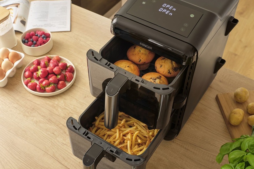 Fritéza horkovzdušná Sencor SFR 1250BK černá Horkovzdušná fritéza Sencor SFR 1250BK s vysunutými dvěma koši ukazuje současnou přípravu různých pokrmů, kdy ve spodním koši jsou hranolky a v horním muffiny. Na kuchyňské lince jsou připravené čerstvé suroviny jako jahody, vejce a brambory.
