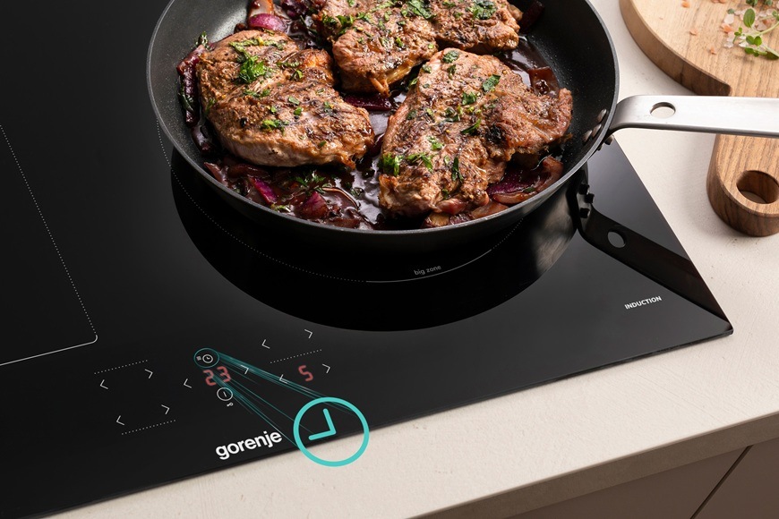 Na indukční varné desce Gorenje GI6431BFG se na pánvi připravuje maso s přesným dotykovým ovládáním výkonu.