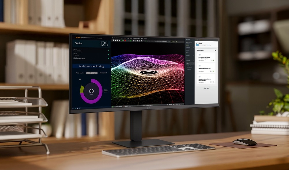 Ultraširokoúhlý monitor na dřevěném stole zobrazuje barevné 3D grafy, data v reálném čase a seznam úkolů. Kancelářské police a složky na rozmazaném pozadí.