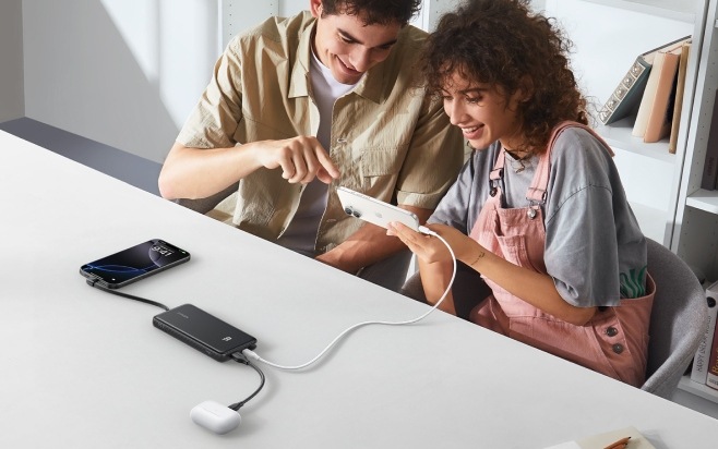 Muž a žena sledují obrazovku smartphonu připojeného k powerbance Anker Zolo společně s dalším telefonem a sluchátky