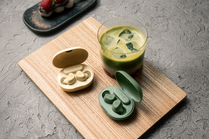 GameBuds Yuzu a Matcha v otevřených pouzdrech na stole vedle nápoje a zákusku