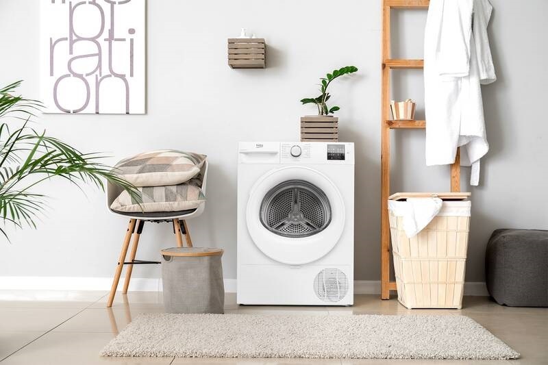 Sušička prádla Beko umístěná v moderním světlém interiéru s dřevěnými doplňky, obrazem, křesílkem a stojanem na prádlo