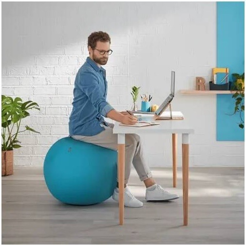 Muž používá sedací míč Leitz Ergo Cosy jako aktivní sezení při práci u stolu