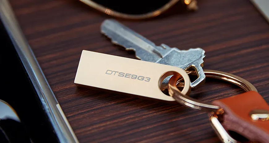 Zlatá varianta USB flashdisku Kingston DataTraveler SE9 G3 připevněná ke klíčům pomocí integrovaného očka, demonstrující snadné přenášení a odolné kovové provedení