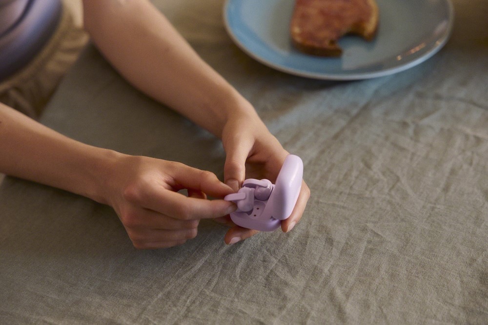 Žena vyndává sluchátka Sony LinkBuds Clip z pouzdra doma na posteli