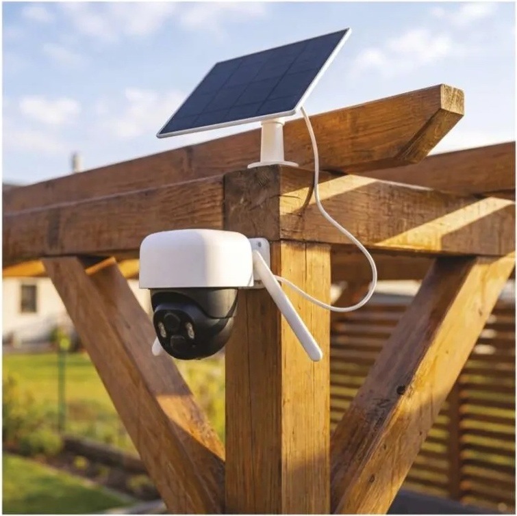 IP kamera EMOS GOSMART venkovní, Wi-Fi IP-1200 WASP 5MPX bílá Otočná kamera EMOS GoSmart je namontovaná na dřevěném sloupku pergoly. Nad ní je solární panel v bílém rámu, propojený s kamerou kabelem pro dobíjení.