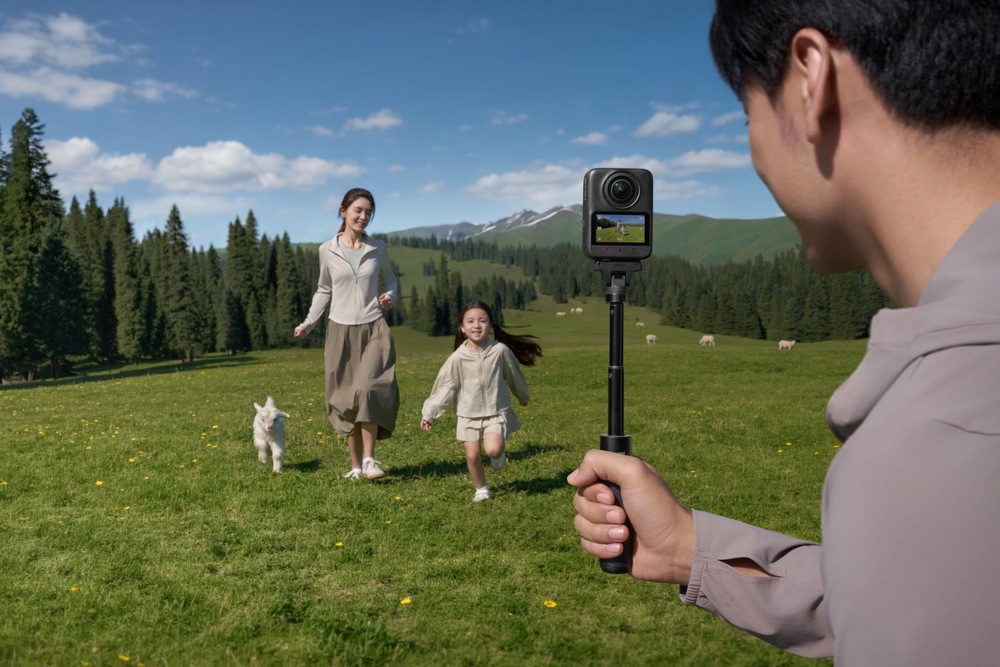 Outdoorová kamera DJI Osmo 360 II Adventure Combo černá Muž držící 360° kameru DJI Osmo 360 II na selfie tyči natáčí ženu s dítětem běžící po horské louce