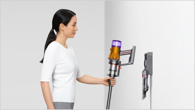 Paní dává tyčový vysavač Dyson V12 Detect Slim Absolute po úklidu do nástěnného držáku, kde bude připravený a vždy po ruce.
