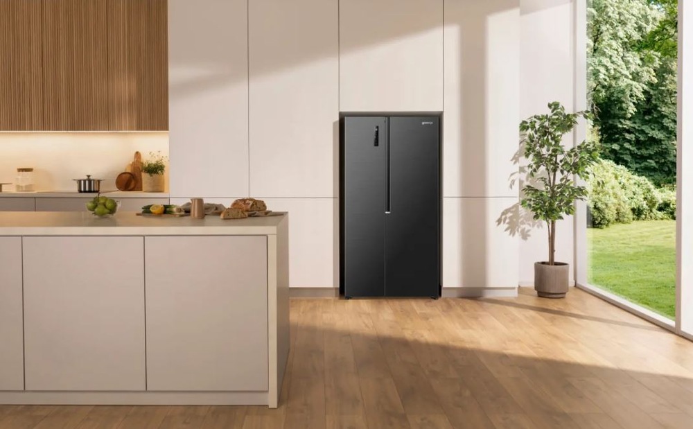 Americká lednice Gorenje G400 NRS917D41BX černá černá americka lednice Gorenje NRS917D41BX umístěná ve světle kuchyni vedle zahrady, která je vidět skrz prosklenou stěnu.