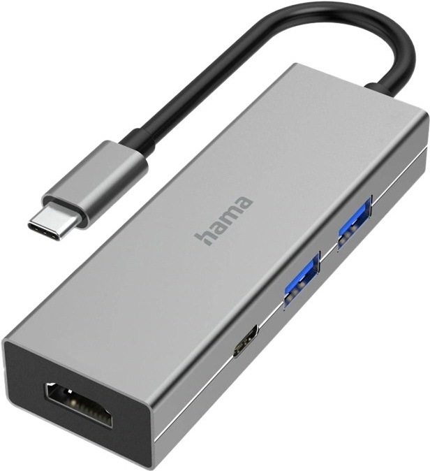 Na obrázku je šedý USB-C hub Hama Multiport zachycený šikmo zepředu. Má úzké kovové tělo s jednoduchým hranatým designem a z jednoho konce z něj vede krátký černý kabel zakončený USB-C konektorem. Na levém čele je HDMI konektor, na boku dva modře označené USB porty a jeden menší USB-C port. Na horní straně je logo hama. Zařízení působí elegantně, kompaktně a je určené pro rozšíření konektivity notebooku nebo tabletu.