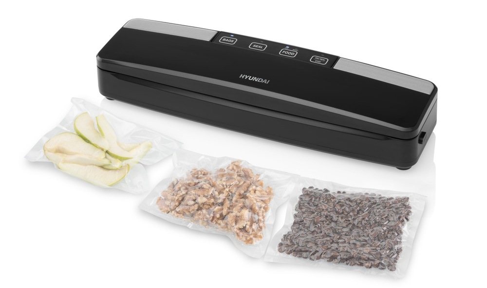 Svářečka fólií Hyundai VS100 černá Černá vakuovačka Hyundai VS 100, vedle které leží tři vakuově zabalené sáčky s potravinami – plátky jablka, vlašské ořechy a lněná semínka