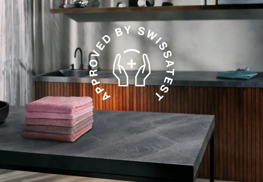 Pračka AEG ProSense™ 6000 LFR61942BC bílá Růžové ručníky složené v komínku na stole. V pozadí linka se dřezem. Nad stolem symbol pro certifikaci Swissatest.