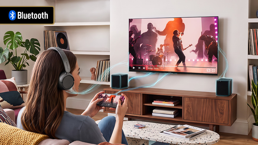 Televize Hyundai HL 327602V Funkce Bluetooth u televizoru: Žena se sluchátky na uších a herním ovladačem v ruce bezdrátově přenáší zvuk z televize a reproduktorů. Logos štítek: Bluetooth.