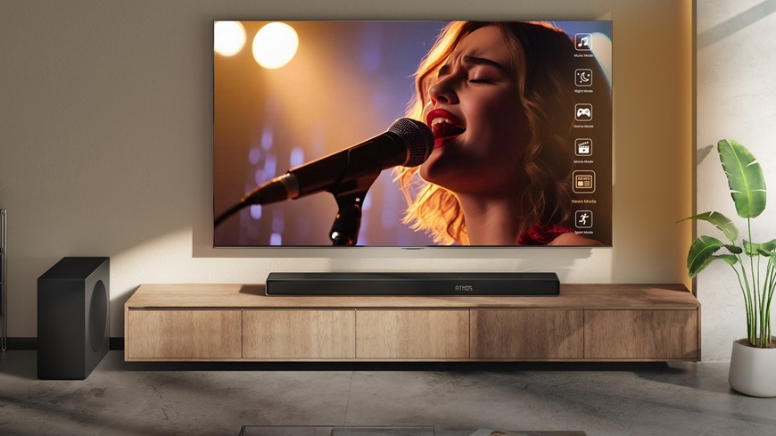 Televize Hisense je připevněná ke stěně. V televizi zpívá paní na mikrofon.