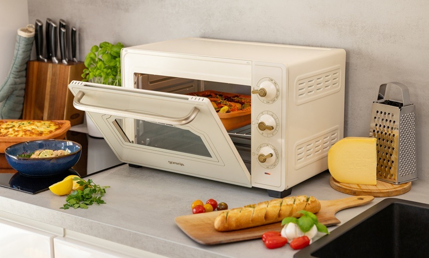 Mini trouba Gorenje OM30CLI má pootevřená dvířka. Kolem ní jsou různé pokrmy.