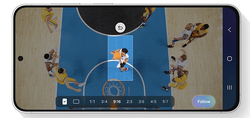 Přední pohled na telefon Galaxy S26 FE v orientaci na šířku, který zachycuje pohled shora na basketbalový zápas. Vertikální rámeček s poměrem stran 9 : 16 zdůrazňuje hráče uprostřed, který se připravuje na střelu, zatímco zbytek obrazovky je ztmavený, což znázorňuje funkci My FanCam sledující vybraný objekt. Panel nástrojů pod obrazovkou zobrazuje možnosti poměru stran 1 : 1, 3 : 4, 9 : 16, 2 : 3, 3 : 5, 4 : 5 a 5 : 7 a vpravo tlačítko Sledovat.
