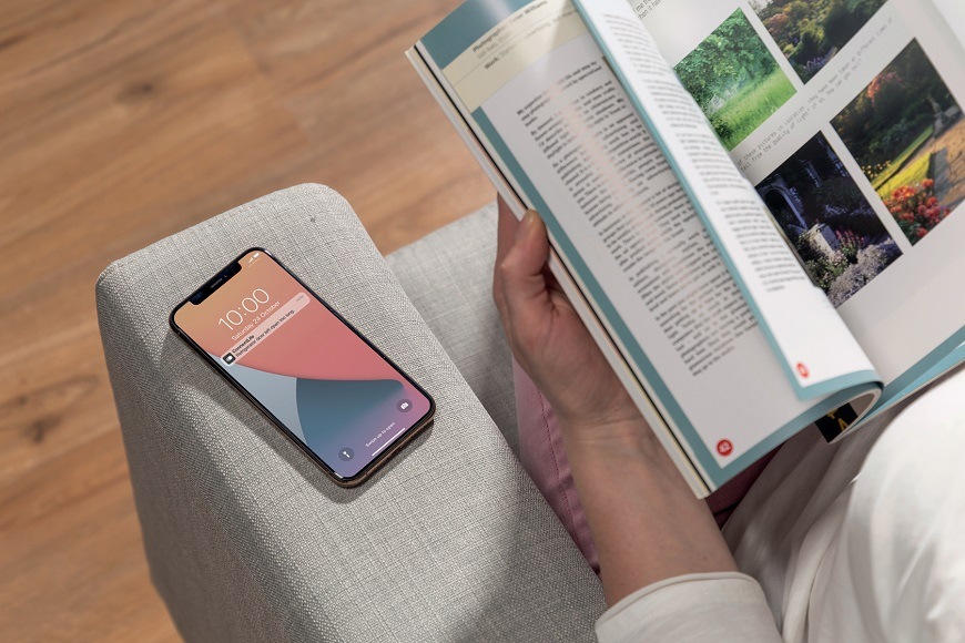 člověk čte knihu s obrazky a vedle něj je na křesle mobilni telefon s notifikaci od ConnectLife.