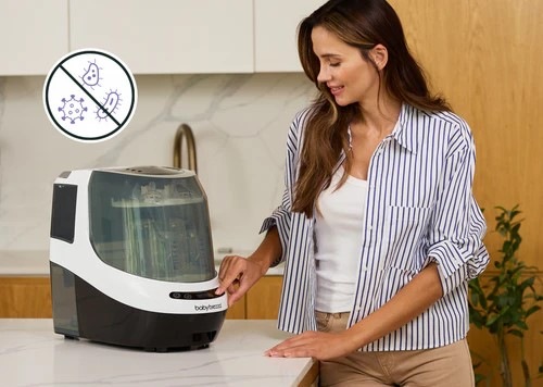 Sterilizátor Baby Brezza Bottle Washer Pro Black černý Sterilizátor Baby Brezza Bottle Washer Pro Black je umístěný v kuchyni, žena do něho vložila dětské příslušenství a nyní ho zapíná stiskem tlačítka.