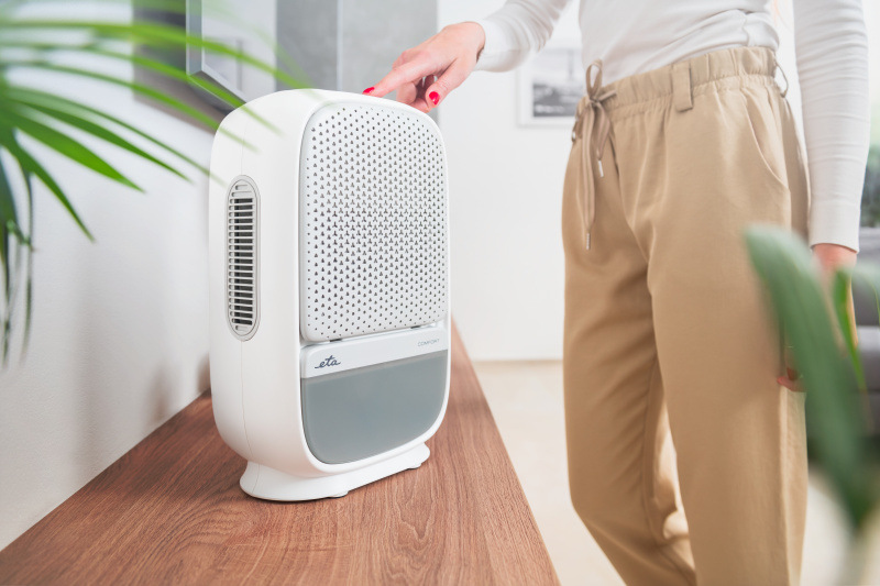 Odvlhčovač ETA Comfort 1630 90000 bílý Modermí bílo-šedý odvlhčovač vzduchu ETA Comfort s perforovanou čelní deskou a integrovanou rukojetí, který je ovládán dotykově ženskou rukou