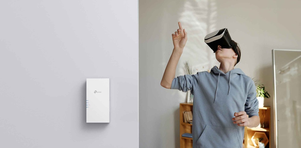 Osoba s nasazeným VR headsetem ukazuje prstem nahoru v místnosti s minimalistickým designem. Na zdi je namontován Wi-Fi extendér TP-Link.