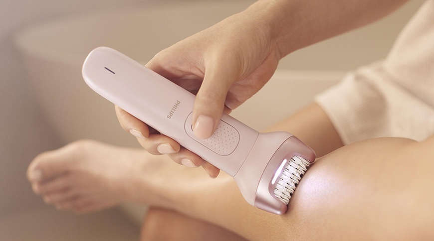 Detail použití epilátoru Philips BRE718/00 v růžové barvě na pokožce nohy, epilační hlavice s osvětlením je přiložená k ošetřované oblasti.