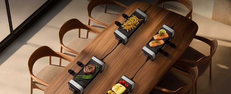 Čtyři propojené raclette grily připravují různé porce podél jídelního stolu